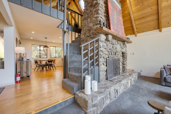 A spacious living area with a stone fireplace, wooden beams, and a dining area with a table and chairs. - Kenwood Vista by Avantstay 7acres w Pool Fire Pit Vineyard Views (Kenwood)