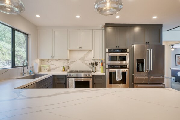 A modern kitchen with white marble countertops, stainless steel appliances, and a large island.