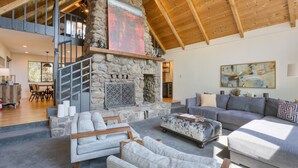 A spacious living area with a stone fireplace, a staircase to an upper level, and a large painting on the wall.
