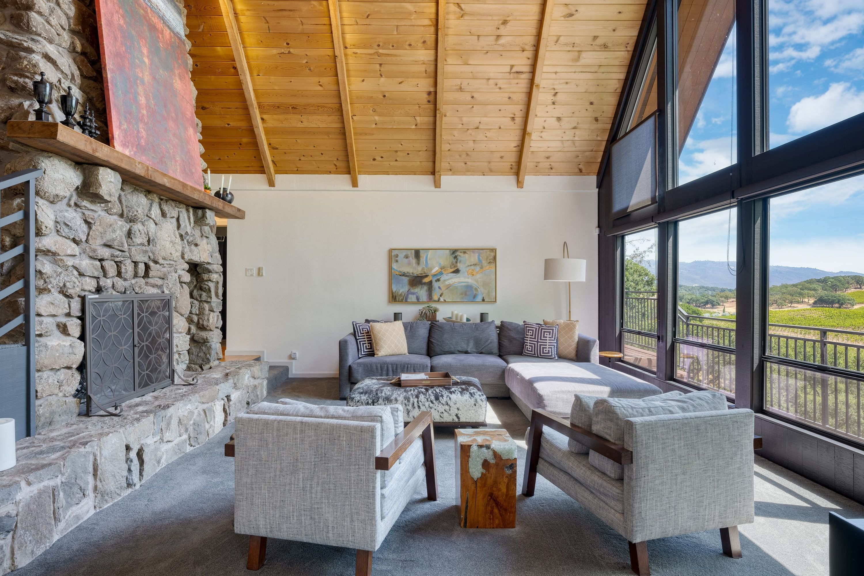 A spacious living room with a stone fireplace, a large window with a view of the countryside, and a cozy seating area with a sofa and armchairs.