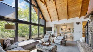 A spacious living area with a high ceiling, large windows, and a cozy seating arrangement.