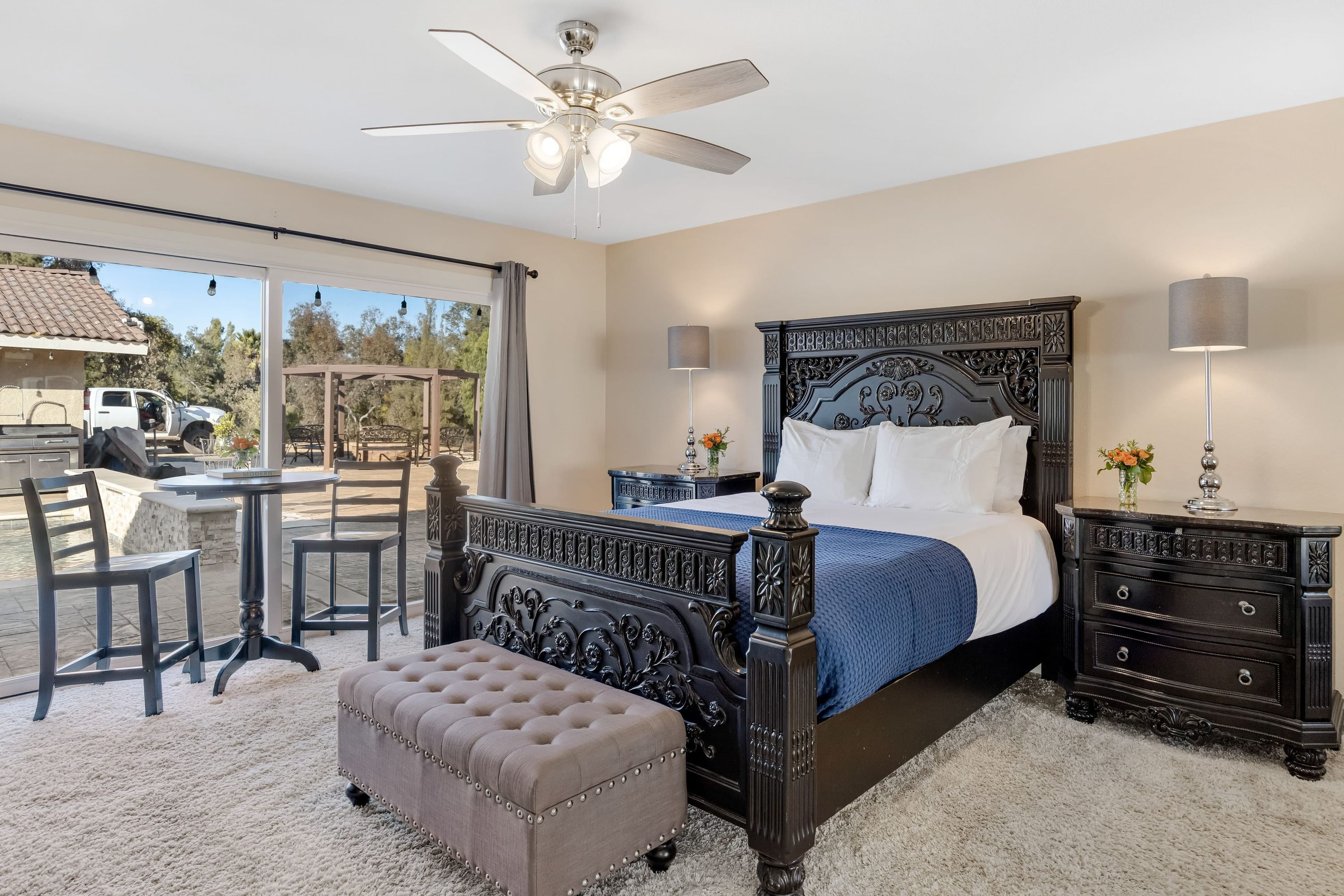 A bedroom with a large bed, a ceiling fan, a small table, and a bench.