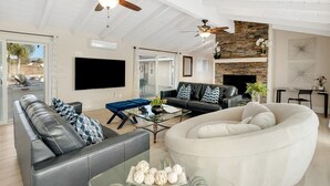 A spacious living room with a large sofa, a coffee table, and a fireplace. There are ceiling fans, a TV, and a stone accent wall.
