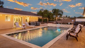 A swimming pool with lounge chairs, a barbecue area, and string lights.