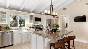 A spacious kitchen with white cabinetry, a granite island, and a large window offering a view of the outdoors.