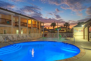 A swimming pool with a white fence, lounge chairs, and a building with balconies.