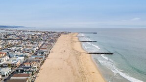 Un paysage urbain côtier avec une longue plage de sable, une jetée s’avançant dans l’eau et des immeubles résidentiels densément regroupés le long de la côte.