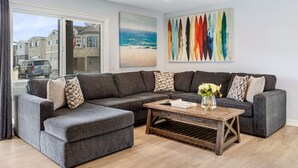 Un salon moderne avec un canapé d’angle gris, une table basse en bois et un tableau sur le thème de la plage.