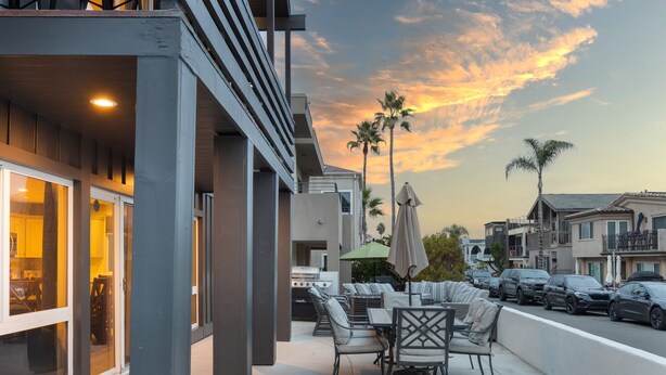 Une terrasse extérieure avec des sièges et un espace barbecue, donnant sur une rue bordée de voitures garées et d’immeubles d’habitation.