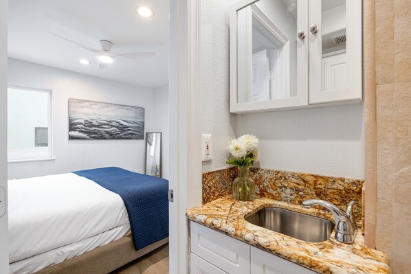 A bedroom with a bed, a nightstand, and a wall-mounted TV. - Sandy by Avantstay Oceanview Steps to Beach Patio w Fire Pit Dining Area (Newport Beach)