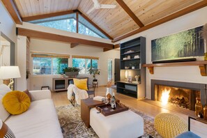 A spacious living room with a fireplace, wooden beams, and large windows. - Sonoma Creek Haven Hot Tub Firepit Creekside Views Near Kenwood Wineries (Kenwood)