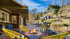 Une terrasse extérieure avec des fauteuils en osier jaune, un foyer et un mur de pierre donnant sur une colline.