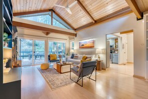 A spacious living area with a high ceiling, wooden beams, a large window, and a view of the outdoors. - Sonoma Creek Haven Hot Tub Firepit Creekside Views Near Kenwood Wineries (Kenwood)