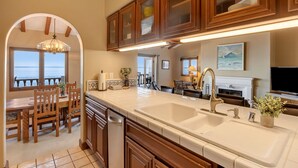 A kitchen with wooden cabinets, a large island with a sink, and a view of the ocean through an archway. - Camino De Flores by Avantstay Views Pool Beach Access Community Amenities (Avalon)
