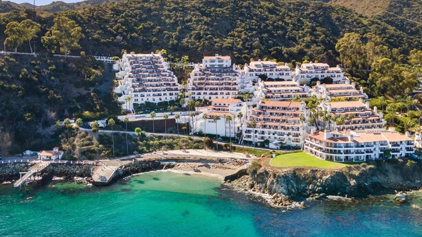 A coastal resort with multi-story buildings, a rocky shoreline, and a mountainous backdrop. - Camino De Flores by Avantstay Views Pool Beach Access Community Amenities (Avalon)