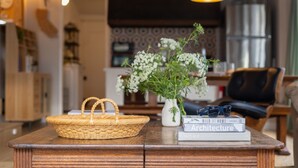 A wooden table with a woven basket, a vase with white flowers, and a stack of books.