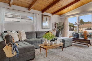 Una sala de estar moderna con un sofá seccional gris, una mesa de centro de madera y un ventanal con vistas al vecindario.