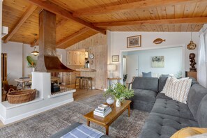 Un espacio habitable amplio con un sofá gris grande, una mesa de centro de madera y una cocina al fondo.