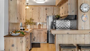 A kitchen with wooden cabinets, a stainless steel refrigerator, a sink, and a clock on the wall.