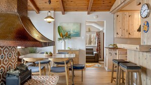 A cozy interior with a wooden ceiling, a dining area with a table and chairs, a kitchen with wooden cabinets, and a clock on the wall.