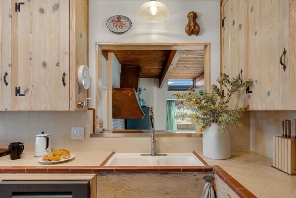 Una cocina moderna con armarios de madera, un fregadero y una encimera con una cafetera, un croissant y un jarrón de flores.