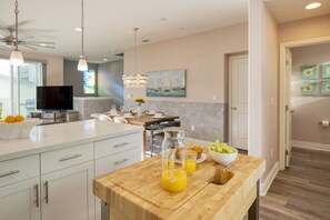 A modern kitchen with a wooden island, a dining area, and a living space with a TV and artwork. - Casa do Sol by Avantstay Rooftop Deck w Ocean Views 2 Blocks to Beach (Pismo Beach)