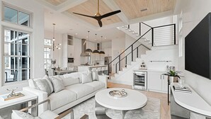 A spacious living area with a white sofa, a round coffee table, and a staircase leading to an upper level. - Katydid Beach Bungalow by Avantstay Gulf Views New Construction in Seagrove (Santa Rosa Beach)