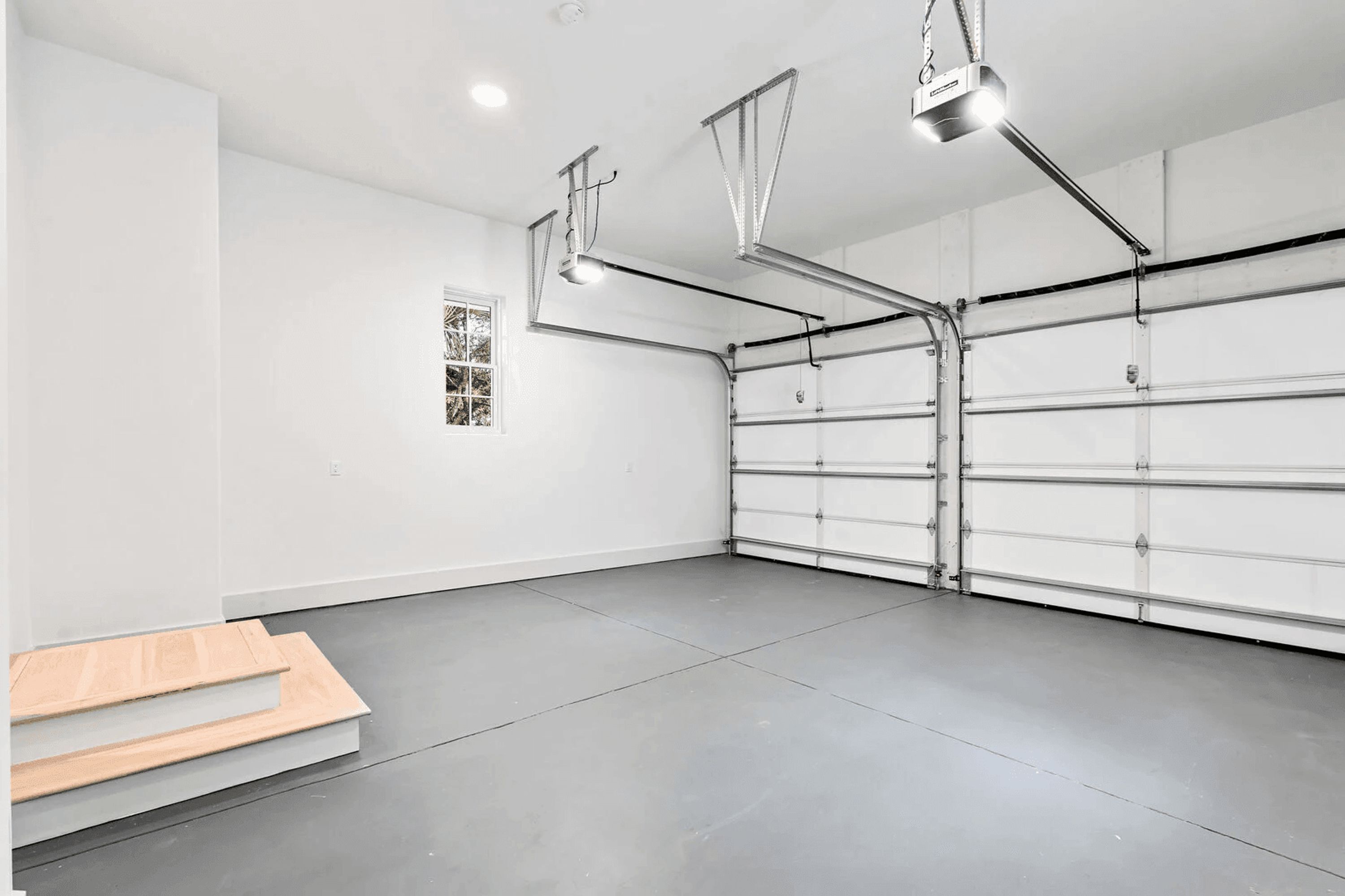 A spacious garage with a clean, modern design, featuring a large white garage door, overhead lighting, and a small window.