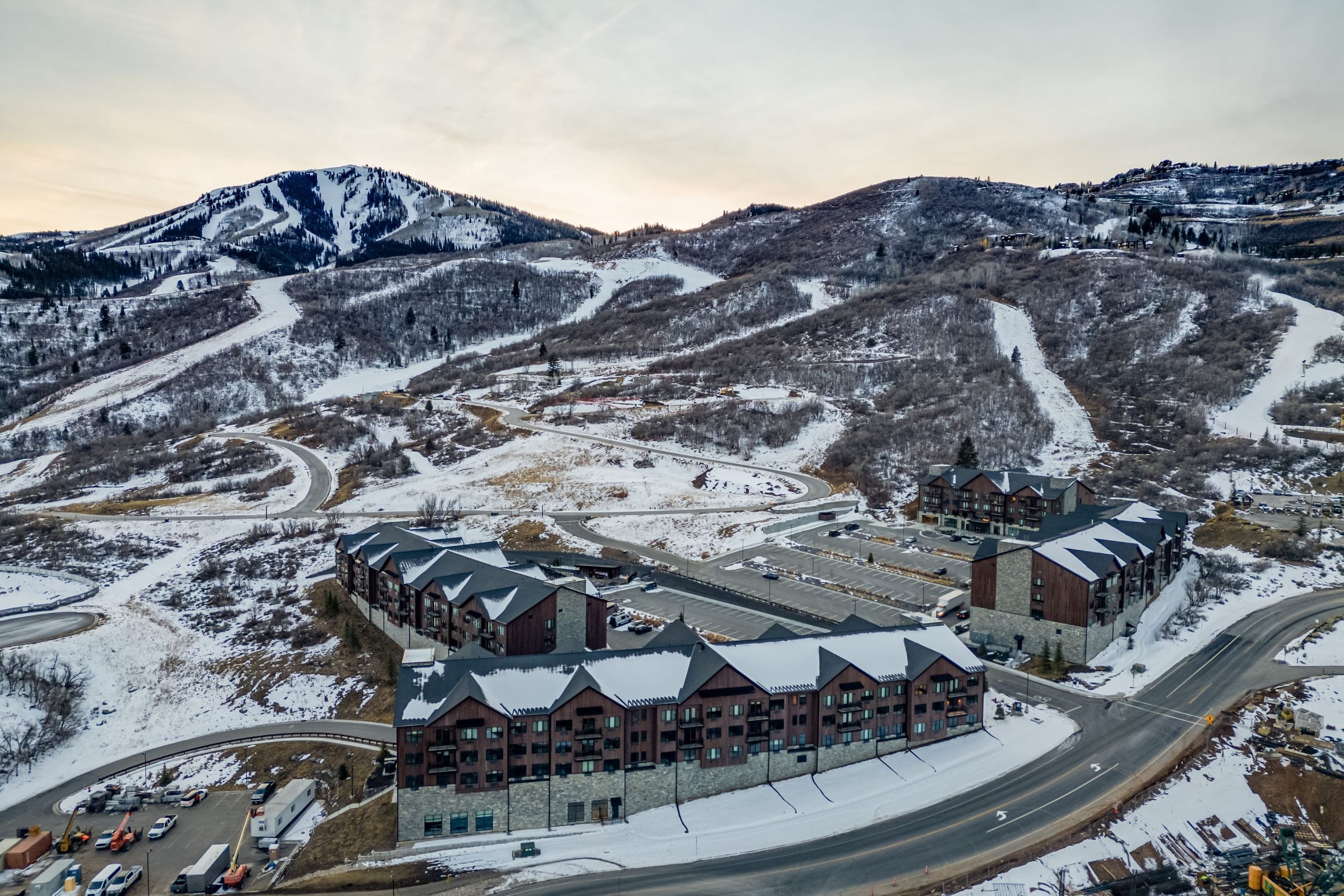 Um hotel de vários andares com design arquitetônico moderno, situado em área montanhosa com um resort de esqui ao fundo.