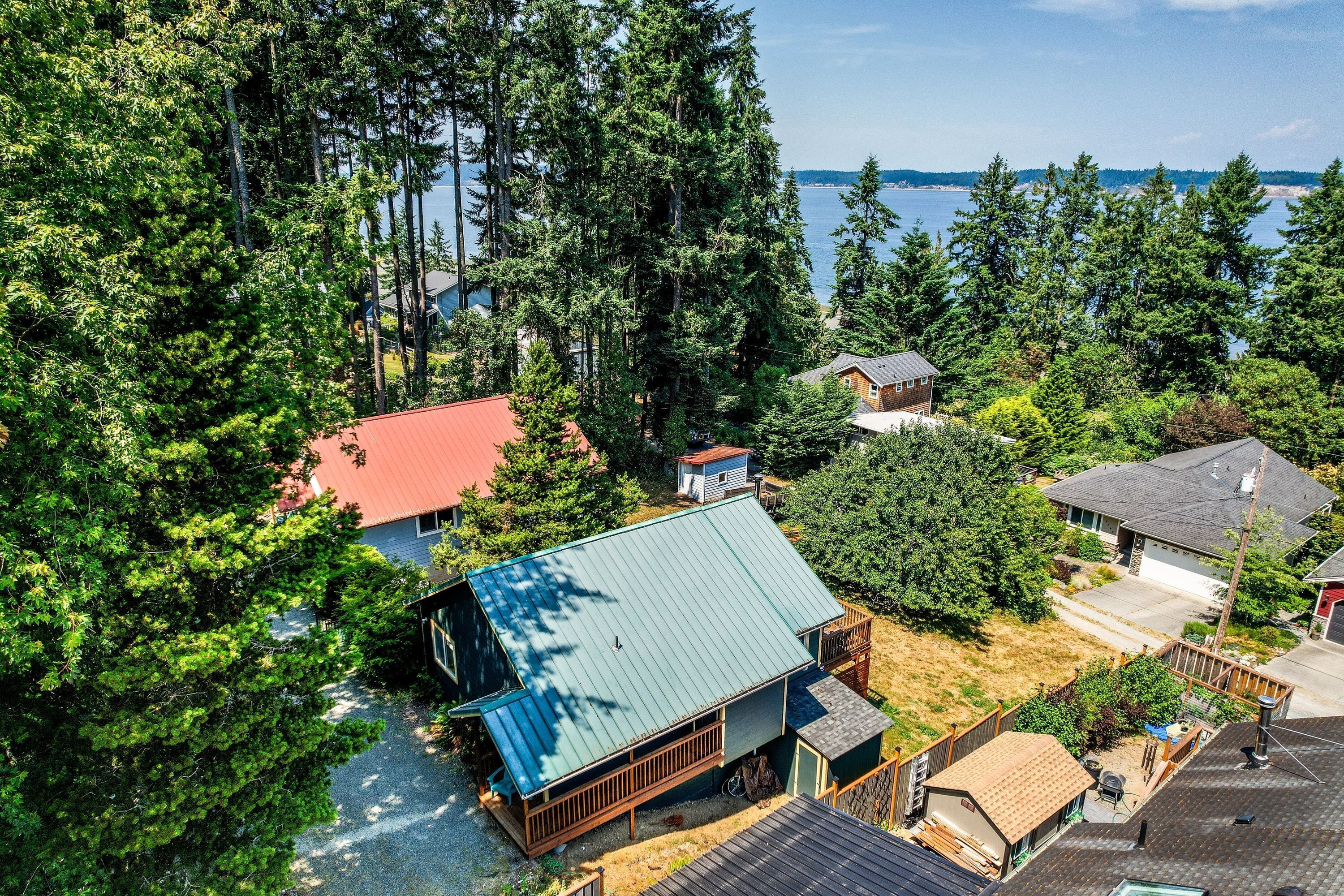 A residential area with a house featuring a green roof, surrounded by dense trees and a view of a body of water.