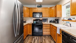 A compact kitchen with wooden cabinets, a stainless steel refrigerator, a black microwave, and a dishwasher. - Seaside Getaway by Avantstay Deck w Views (Langley)