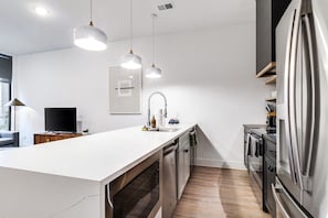 Une cuisine moderne dotée d’un grand îlot central, d’appareils électroménagers en acier inoxydable, de luminaires suspendus et d’un four encastré.