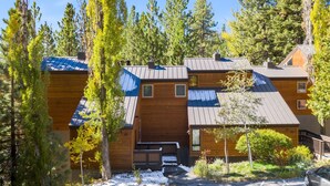 Una baita con facciata in legno, diverse finestre e una zona relax all'aperto coperta.