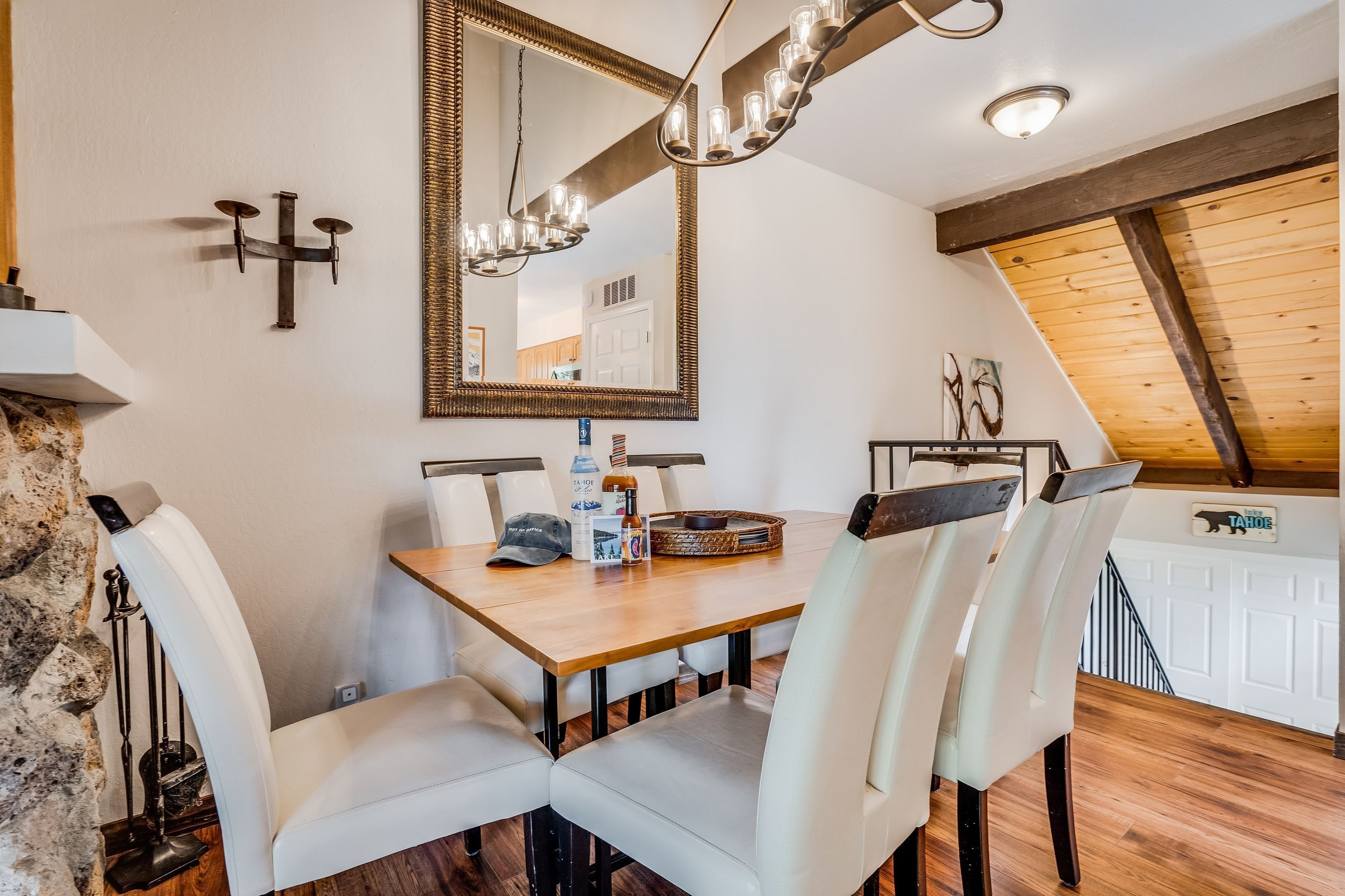 A dining area with a wooden table, white chairs, a chandelier, and a large mirror on the wall.