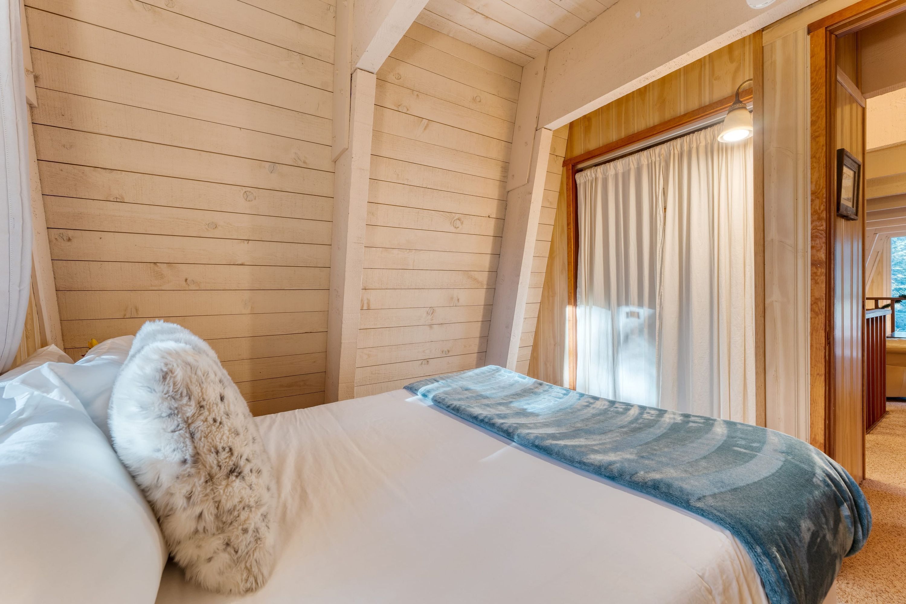 A wooden-paneled room with a bed, white bedding, and a view through a window with curtains.