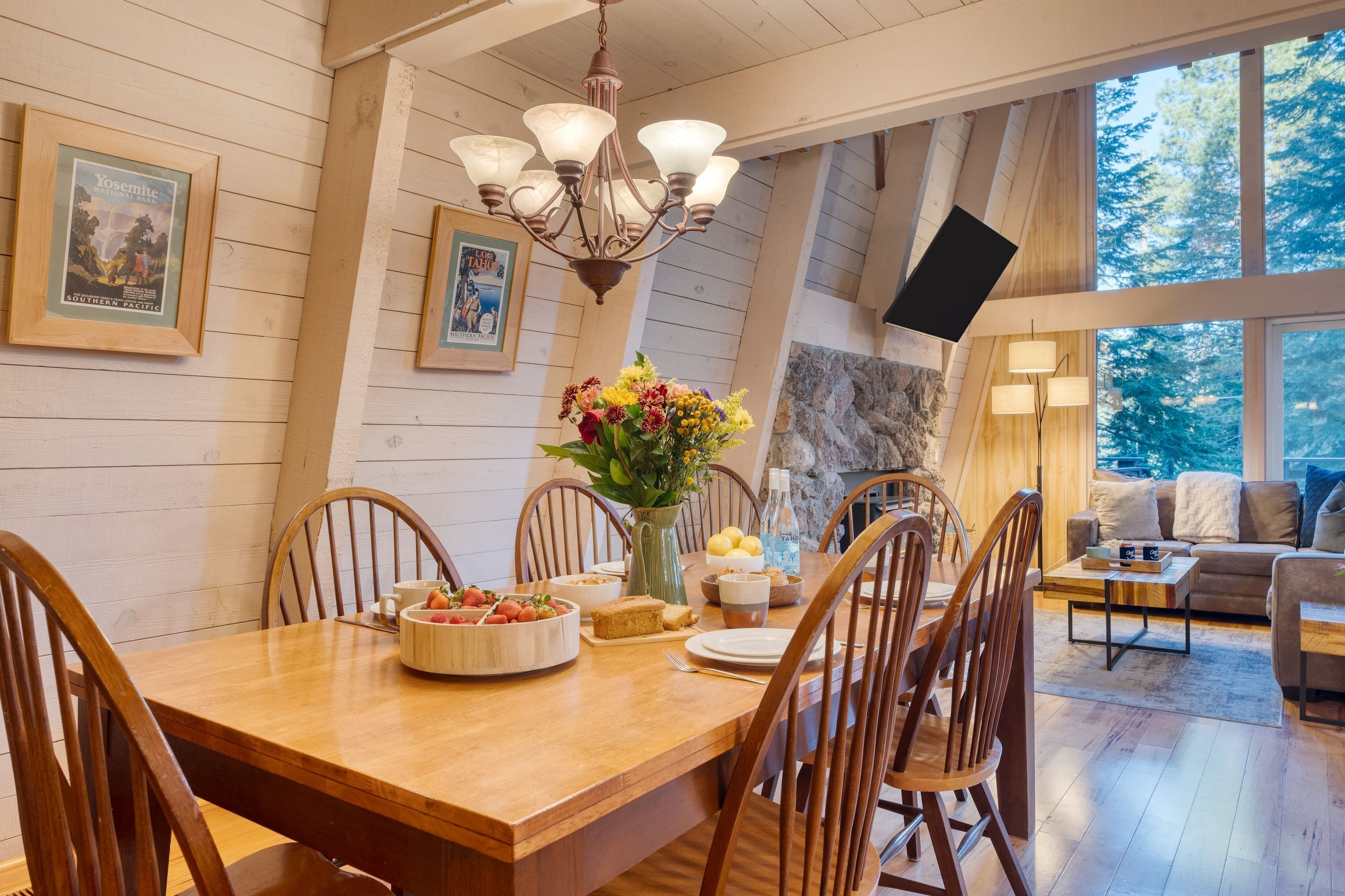 A dining area with a wooden table, chairs, a chandelier, and a vase of flowers.