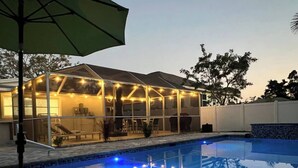 A covered outdoor area with string lights, a pool, and a patio with chairs and tables.