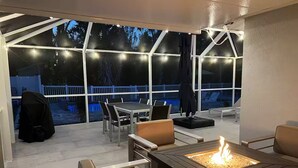 An outdoor patio with a fire pit, seating, and large windows overlooking a backyard.