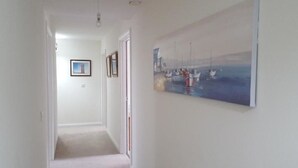 Een gang met een schilderij van boten aan de muur, een lijst met een foto aan de wand en een vloerbedekking.