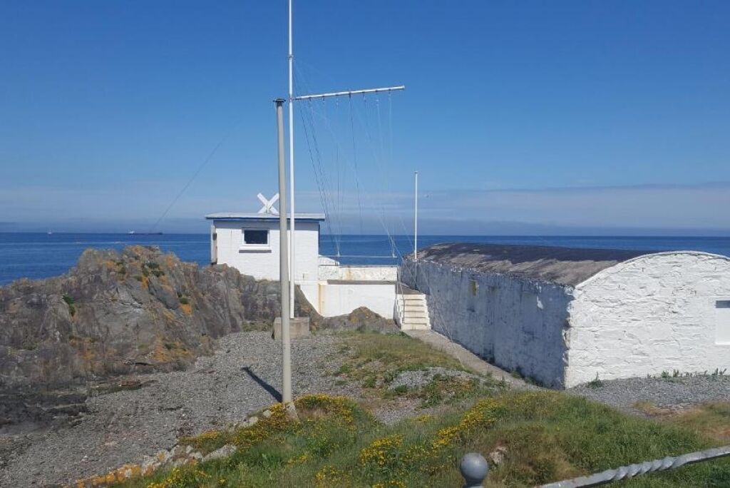 A coastal building with a white exterior, a small tower, and a stone wall.