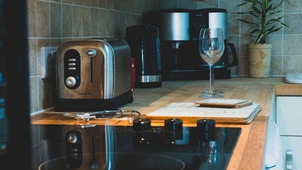 Een keuken met een broodrooster, koffiezetapparaat en een glas wijn op het aanrecht.