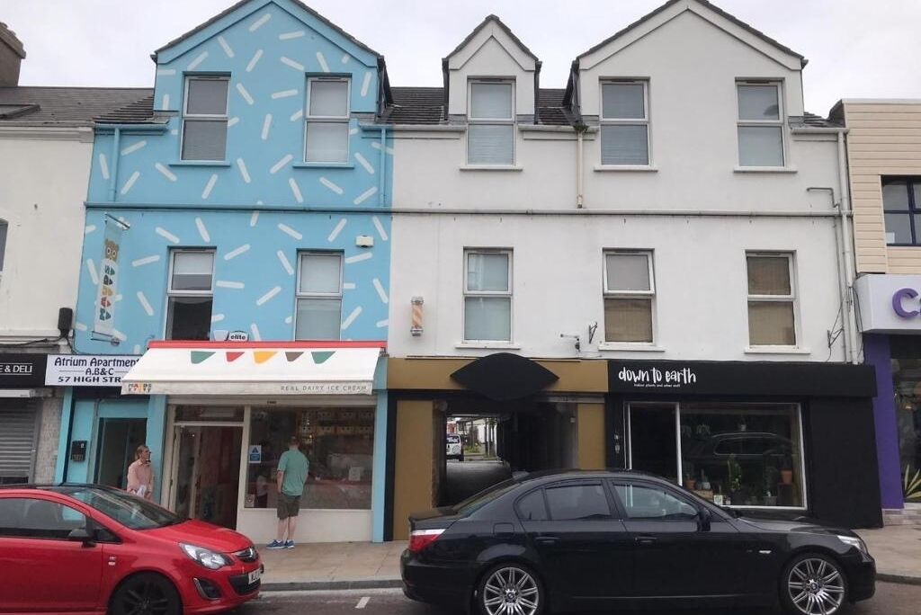 A row of buildings with a blue building featuring a clock pattern, a white building, and a black storefront with a sign reading "down to earth."