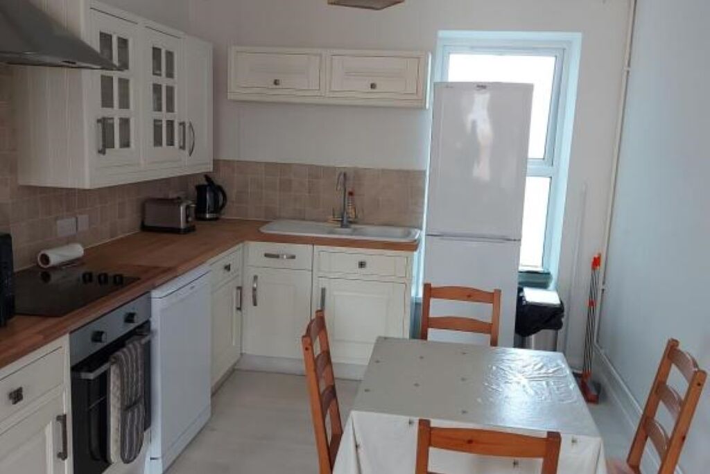 A compact kitchen with white cabinets, a built-in oven, a sink, and a table with chairs.