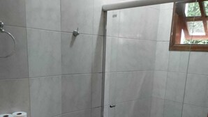 A small bathroom with a shower stall, toilet, and a shelf with toilet paper. - Pousada Santo Antônio (Santo Antonio do Pinhal)