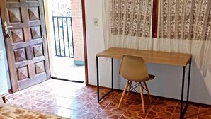 A room with a wooden desk, a chair, a patterned floor, a door, and a window with curtains. - Pousada Santo Antônio (Santo Antonio do Pinhal)
