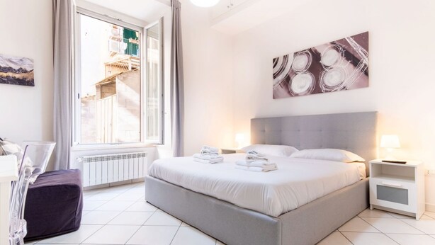 A modern bedroom with a large bed, a nightstand, a window with a view of a building, and a painting on the wall. - Elegantis Giolitti Suite Apartment with Private Balcony (Roma)