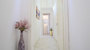 A narrow hallway with a tiled floor, a vase with flowers, and a painting on the wall. - Elegantis Giolitti Suite Apartment with Private Balcony (Roma)