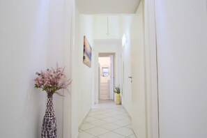 A narrow hallway with a tiled floor, a vase with flowers, and a painting on the wall.