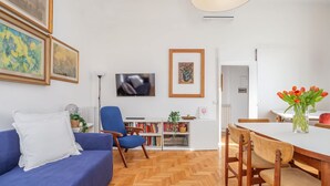Un saló amb un sofà, una televisió, una biblioteca i una zona de menjador amb caires i una taula.
