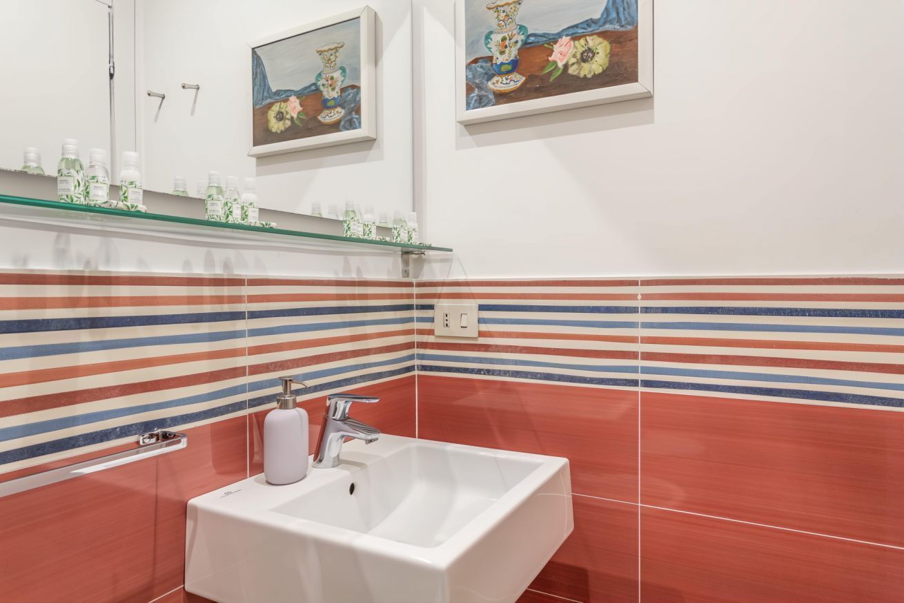 Une salle de bain avec un lavabo blanc, des carreaux muraux à rayures et deux tableaux encadrés au-dessus du miroir.